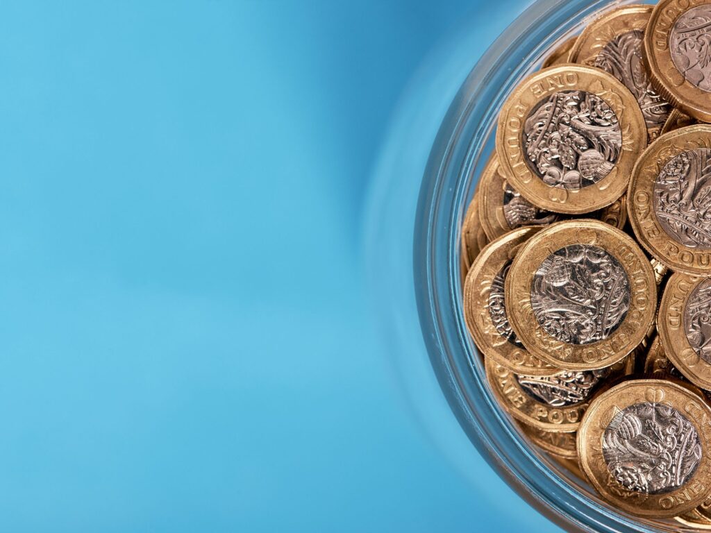 Bowl of pound coins on a blue background.