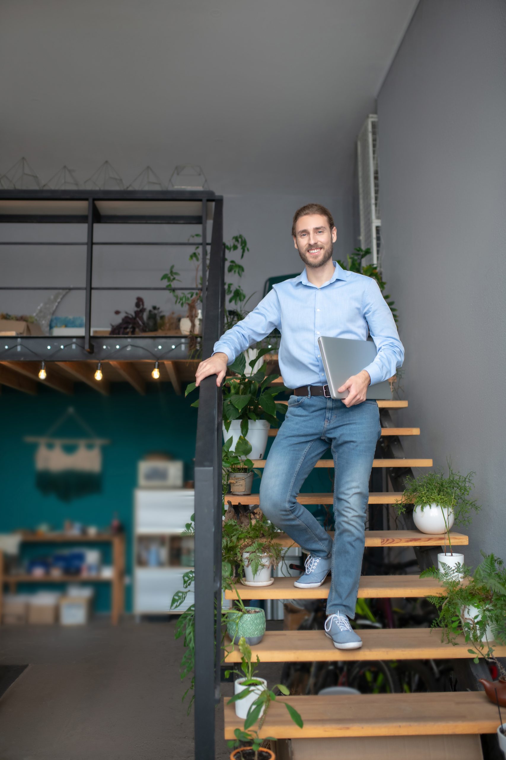 Out of office. A man standing on the wooded stairs and holding his laptop